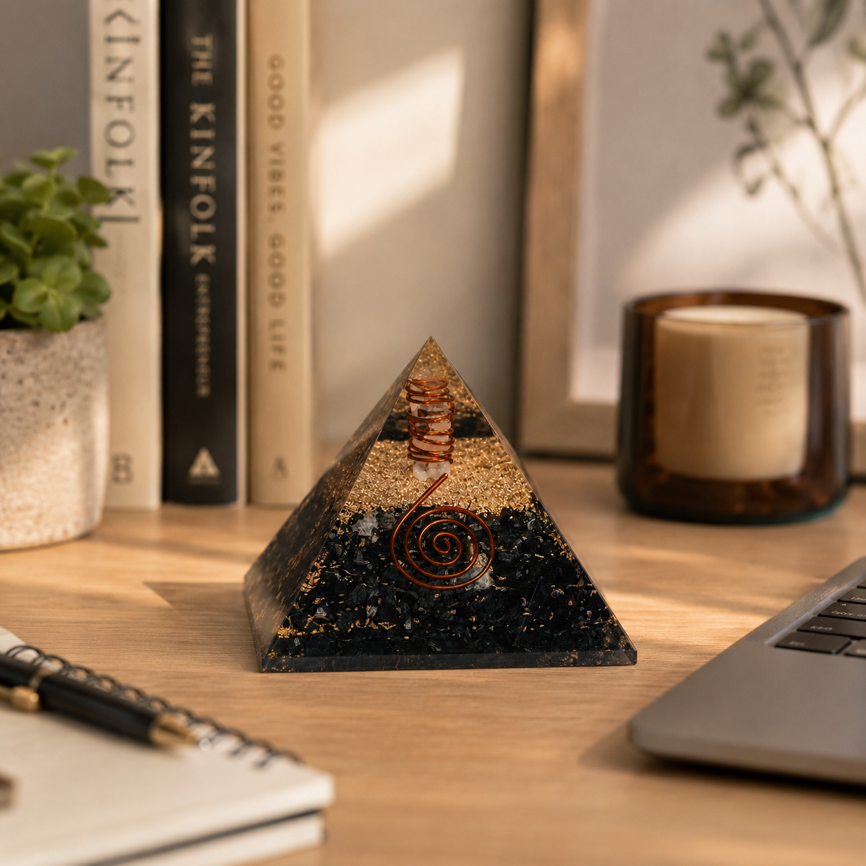 Black tourmaline orgonite pyramid displayed on mindful workspace desk with notebook, plant, and warm natural lighting.